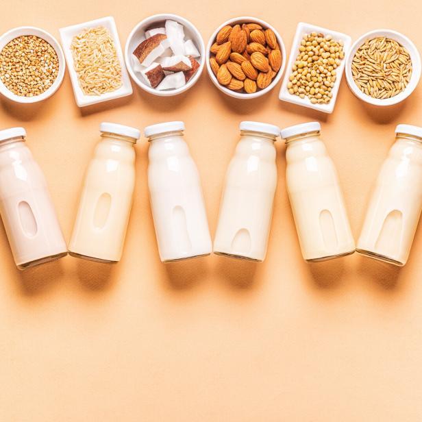 Verschiedene Milchalternativen in Glasflaschen und Schüsseln mit Zutaten wie Mandeln und Sojabohnen.