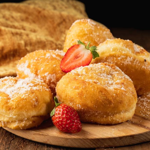 Eine Gruppe von Krapfen, bestreut mit Zucker, garniert mit Erdbeeren auf einem Holzbrett.