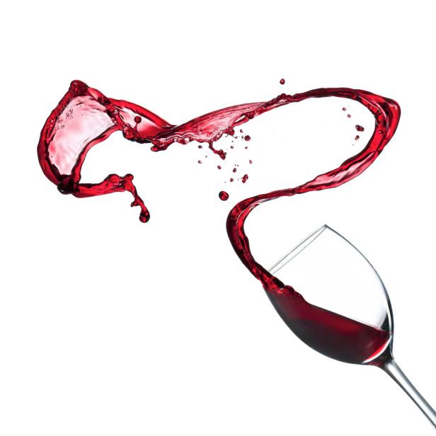 Rotwein spritzt aus einem Glas vor einem weißen Hintergrund.