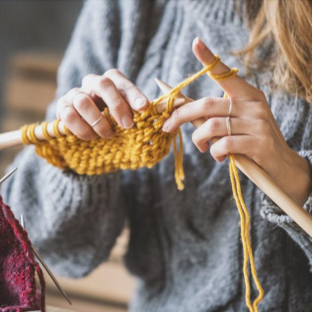 Eine Person strickt mit gelber Wolle an einem Strickprojekt.