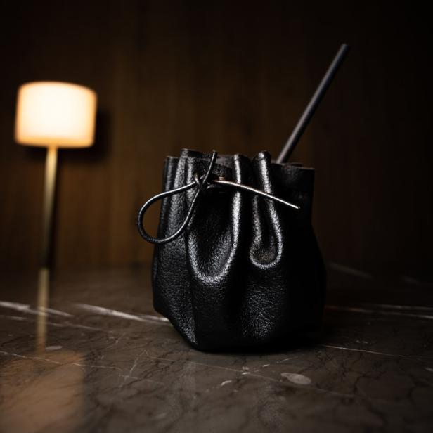 Ein schwarzer Cocktail in einem Lederbeutel mit einem Strohhalm auf einem Tisch.