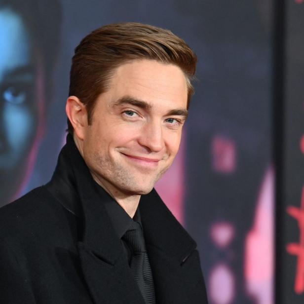 Robert Pattinson posiert vor einem Hintergrund mit Fragezeichen für den Film „The Batman“.