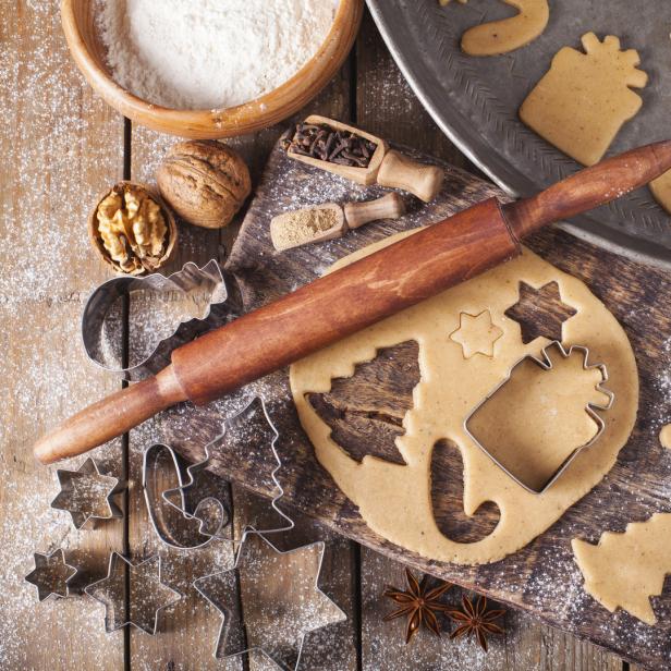 Auf einem Holztisch liegen Teig, Ausstechformen und Zutaten für Weihnachtsplätzchen.