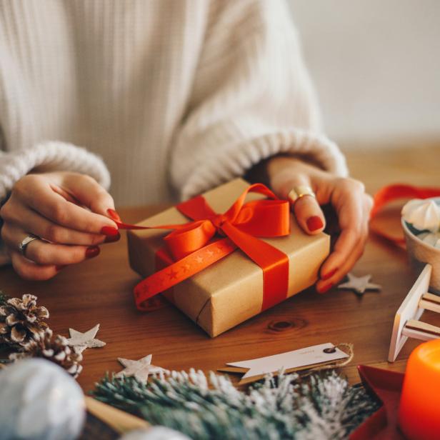 Eine Frau bindet eine rote Schleife um ein Geschenk auf einem Tisch mit Weihnachtsdekorationen.