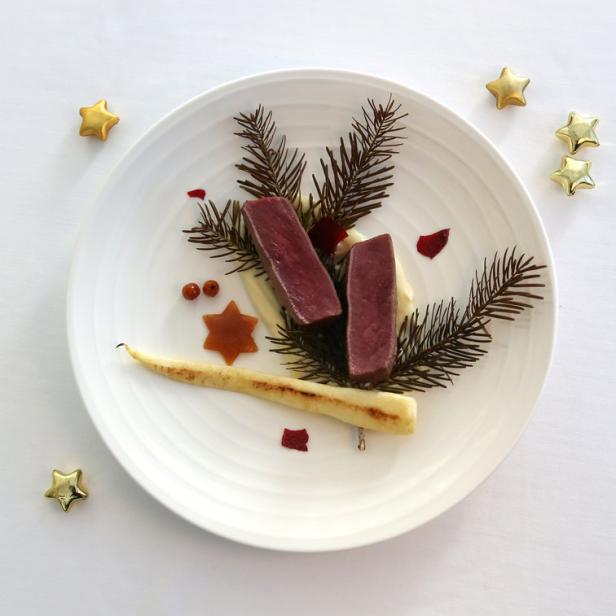 Ein festlicher Teller mit rosa gebratenem Fleisch, Pastinake und Tannenzweigen dekoriert.