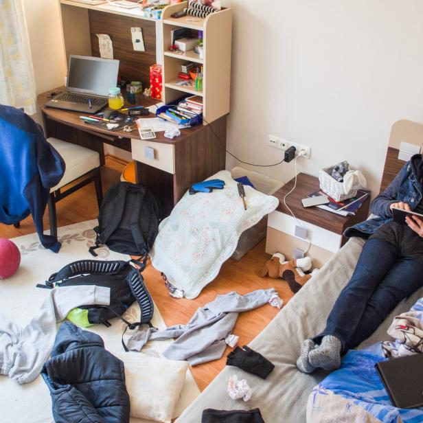 Ein Jugendlicher sitzt mit Kopfhörern und Tablet in einem unordentlichen Zimmer.