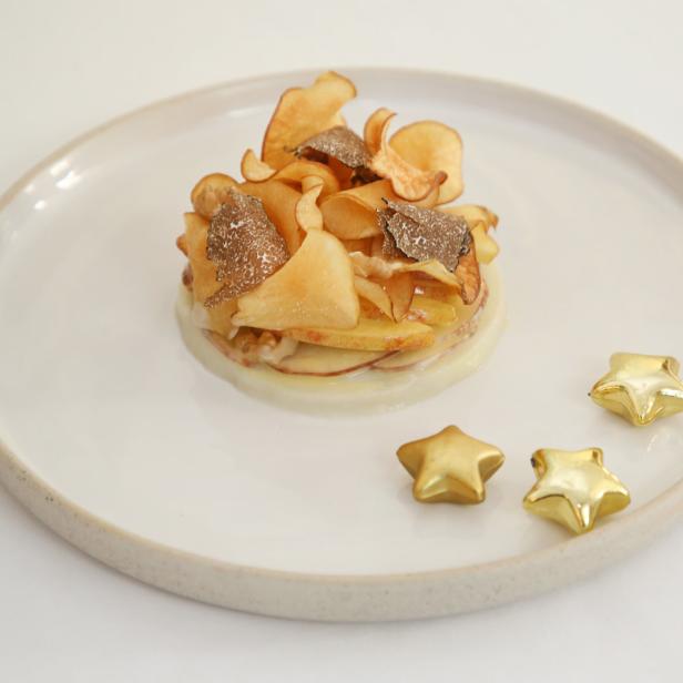 Ein Teller mit einem kunstvoll angerichteten Gericht aus Kartoffelchips und Trüffeln, dekoriert mit goldenen Sternen.