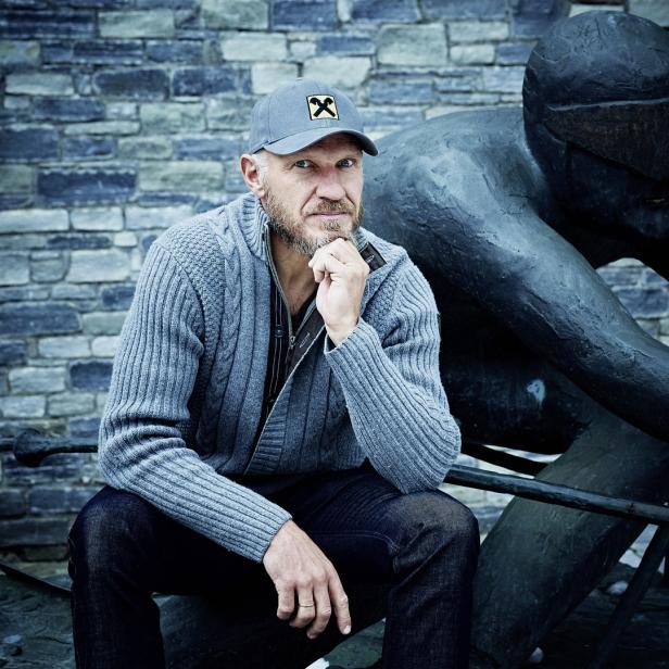 Ein Mann sitzt neben einer Statue des österreichischen Schwimmers Hermann Maier.