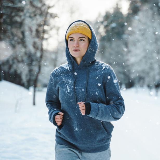 Eine Frau mit gelber Mütze joggt im Schnee.