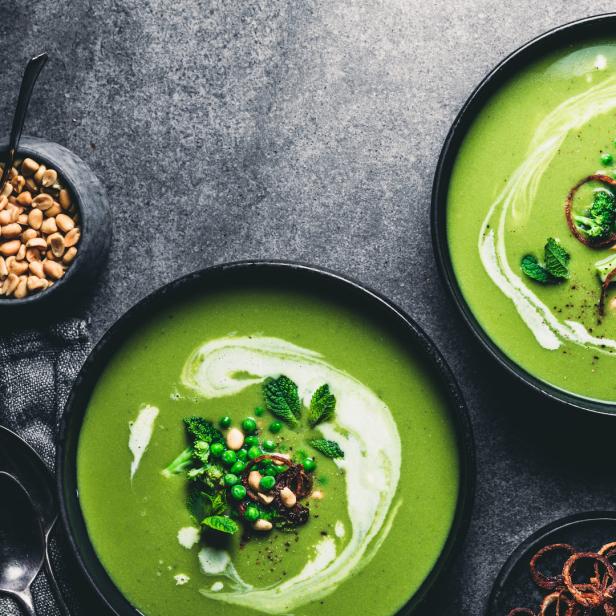 Zwei Schalen mit grüner Erbsensuppe, garniert mit Minze und gerösteten Zwiebeln.