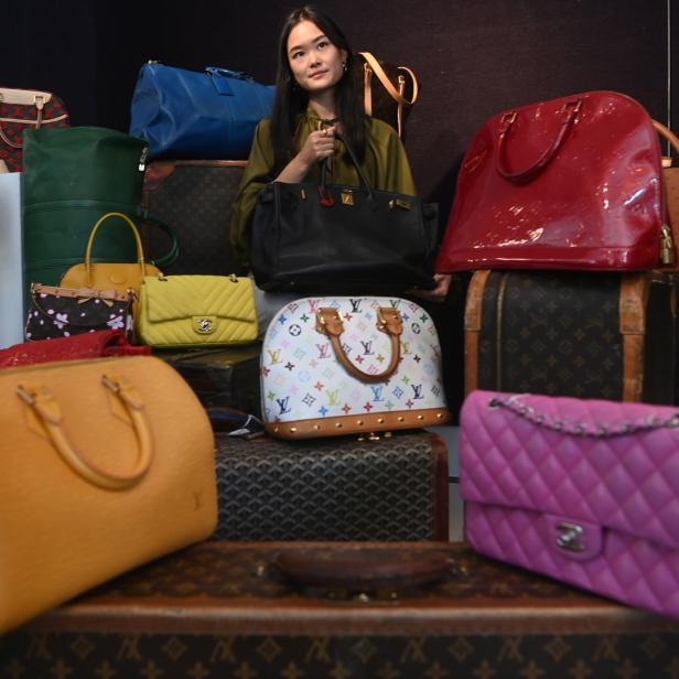 Eine Frau steht umgeben von einer Sammlung verschiedener Handtaschen und Koffer.