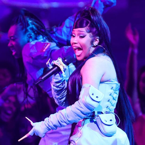 Cardi B tritt in einem hellblauen Outfit mit einem Mikrofon in der Hand auf einer Bühne auf.