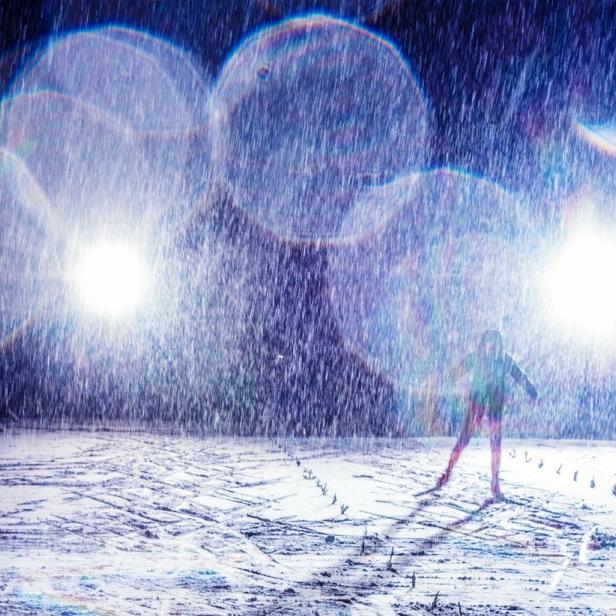 Eine Person steht im Schnee unter hellem Licht und starkem Schneefall.
