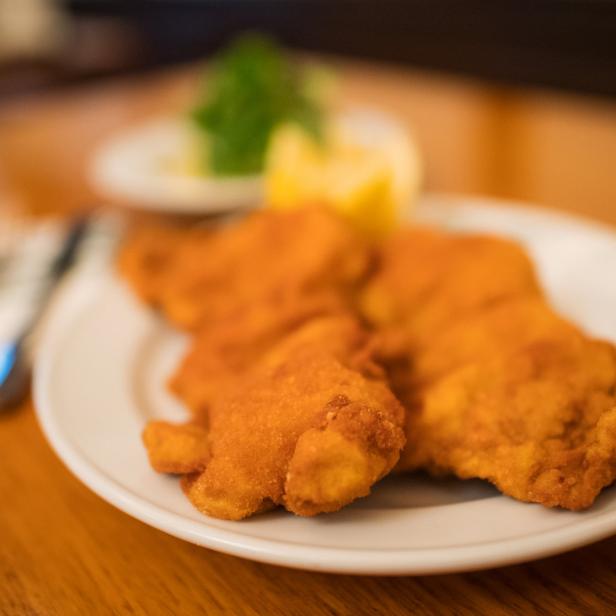 Zwei goldbraune Schnitzel liegen auf einem weißen Teller mit Zitrone und Petersilie.