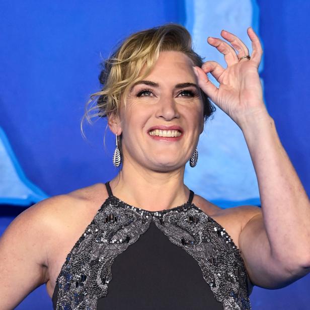 Kate Winslet lächelt und formt mit der Hand eine „Okay“-Geste.