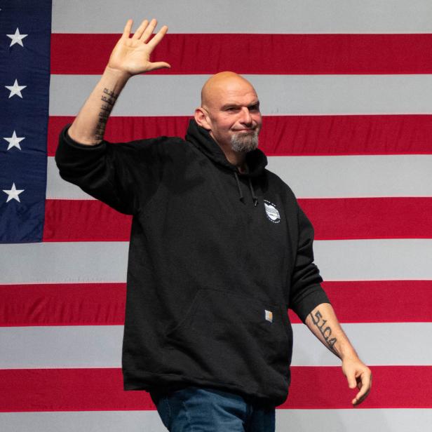 John Fetterman steht vor der US-Flagge und winkt.
