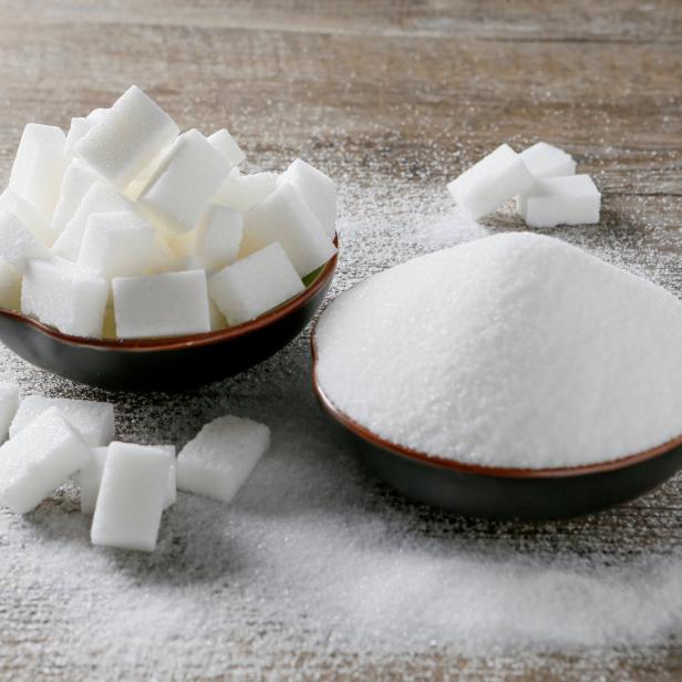 Zwei Schalen, eine mit Zuckerwürfeln und eine mit Zucker, stehen auf einem Holztisch.