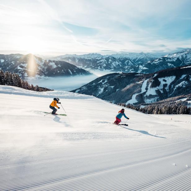 Zwei Skifahrer auf der Piste in Schmittenhöhe Zell am See vor verschneiten Bergen.