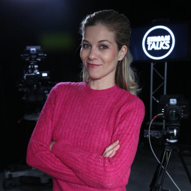 Eine Frau mit verschränkten Armen steht vor Kameras und einem „Stream Talks“-Logo.