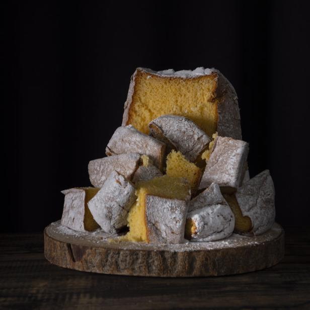 Ein angeschnittener, mit Puderzucker bestäubter Pandoro auf einem Holzbrett.