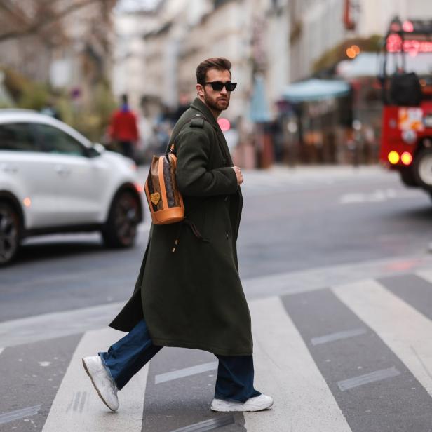 Ein Mann mit Sonnenbrille und Rucksack überquert eine Straße.