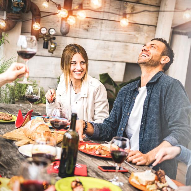 Eine Gruppe von Freunden genießt ein Essen im Freien mit Wein und guter Stimmung.