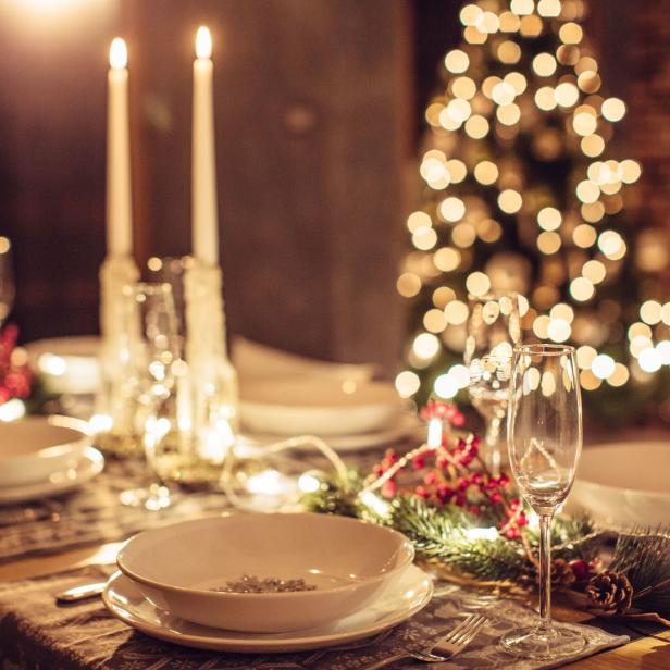 Ein festlich gedeckter Tisch mit Tellern, Gläsern, Kerzen und einem Weihnachtsbaum im Hintergrund.