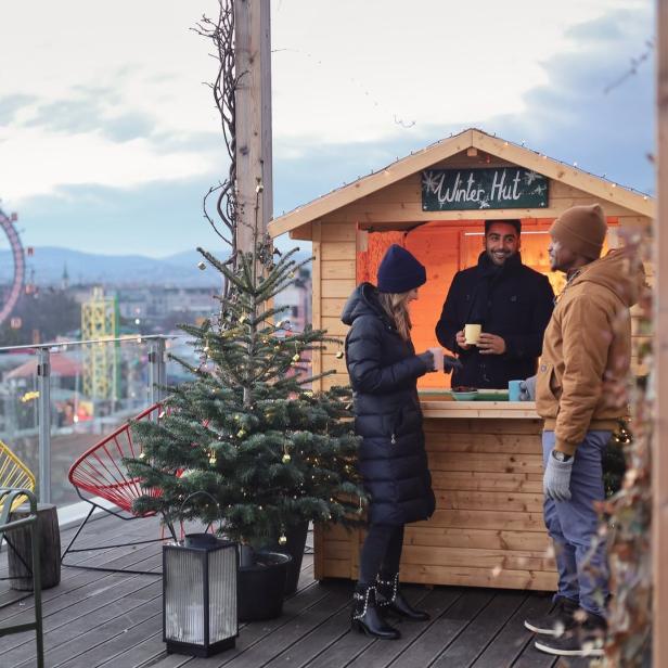 Auf einer Dachterrasse besuchen Menschen eine „Winter Hut“ mit Blick auf Wien.