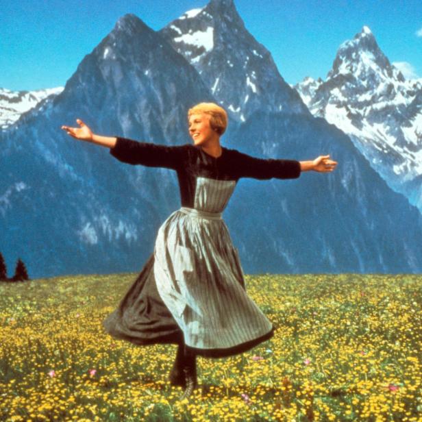 Julie Andrews als Maria tanzt auf einer Blumenwiese vor einer Bergkulisse im Film „The Sound of Music“.
