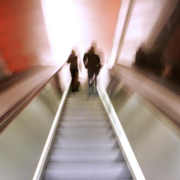 Zwei Personen fahren mit einer Rolltreppe nach oben.