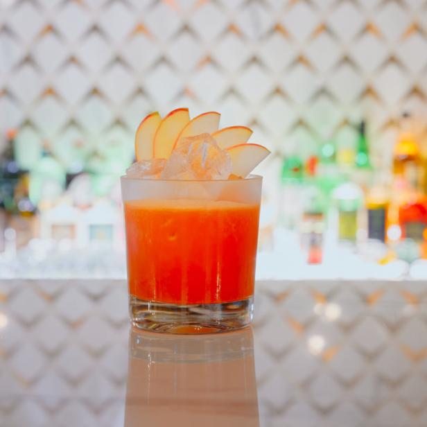 Ein orangefarbener Cocktail mit Eis und Apfelscheiben auf einer Bar.