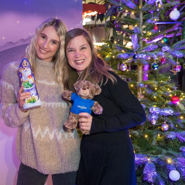 Zwei Frauen posieren mit einem Schokoladen-Nikolaus und einem Teddybär vor einem Weihnachtsbaum.
