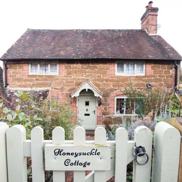 Das „Honeysuckle Cottage“ ist ein kleines Haus mit einem weißen Lattenzaun.
