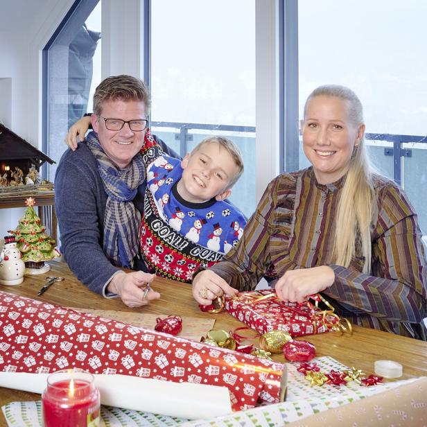 Eine Familie sitzt an einem Tisch und packt Weihnachtsgeschenke ein.
