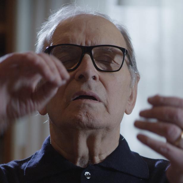 Ein älterer Mann mit Brille gestikuliert mit geschlossenen Augen.