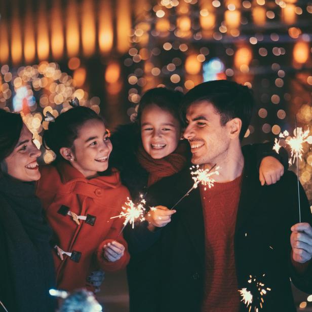 Eine Familie feiert mit Wunderkerzen vor einem Hintergrund aus Lichtern.