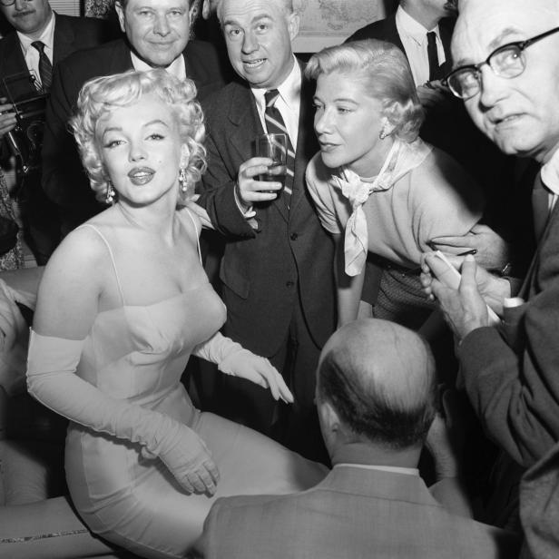 Marilyn Monroe, umgeben von Menschen, sitzt auf einem Sofa.