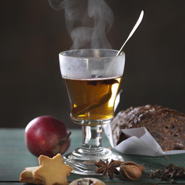 Ein Glas heißer Tee mit Apfel, Gebäck und Gewürzen auf einem Tisch.