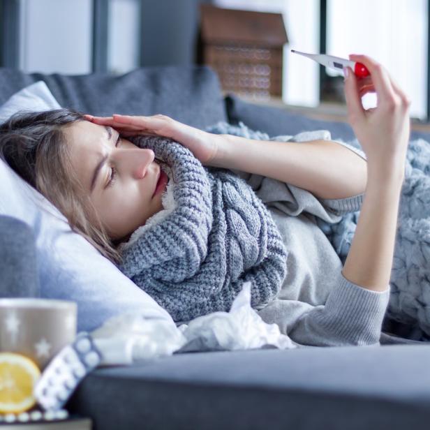 Erkältete Frau mit Husten hält Thermometer in die Höhe.