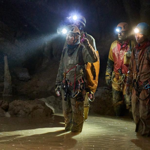 Eine Gruppe von Höhlenforschern watet durch das Wasser in einer dunklen Höhle.