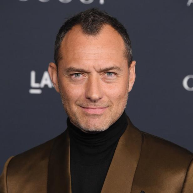 Porträt von Jude Law in einem braunen Anzug mit schwarzem Rollkragenpullover.