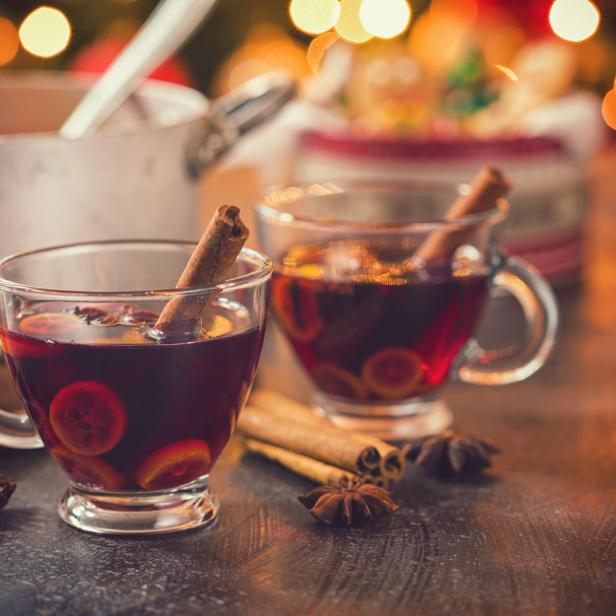 Zwei Tassen Glühwein mit Zimtstangen und Orangenscheiben auf einem Tisch.