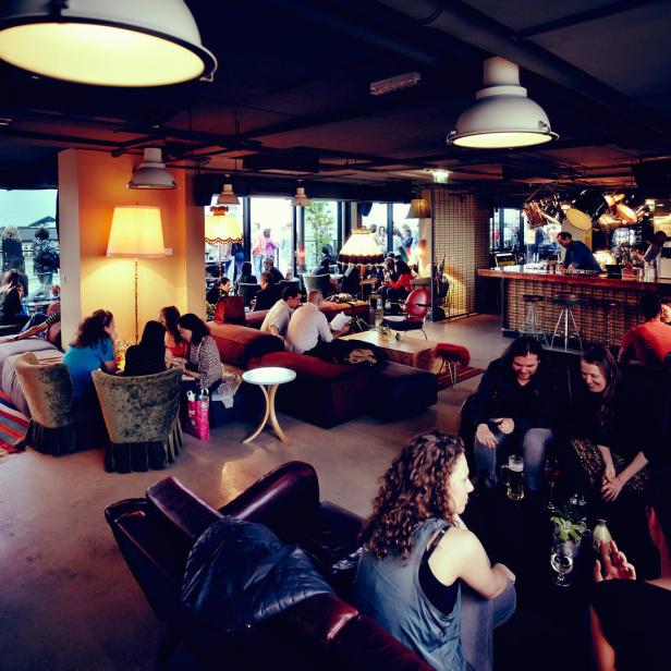 Mehrere Personen sitzen und stehen in einer Bar oder einem Lounge-Bereich.