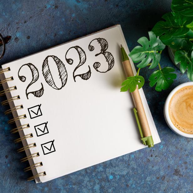 Ein Notizbuch mit der Aufschrift „2023“ und angekreuzten Kästchen liegt neben einer Tasse Kaffee.