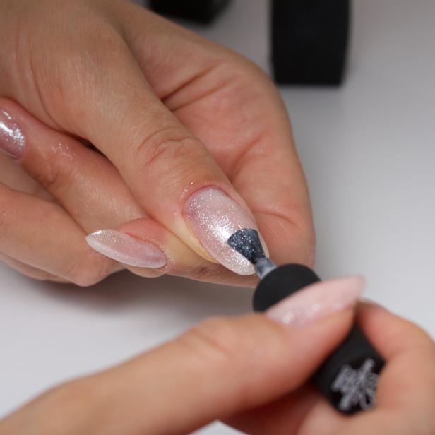 Eine Frau lackiert ihre glitzernden, mandelförmigen Nägel.