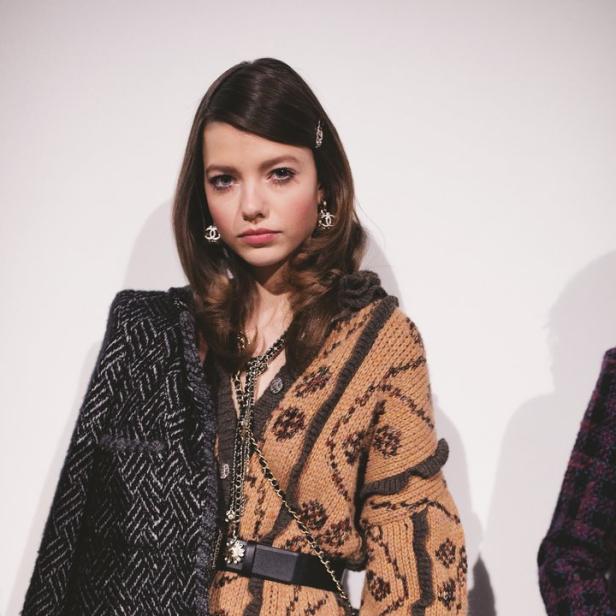 Ein Model trägt einen gemusterten Cardigan mit Gürtel und eine Jacke über der Schulter.