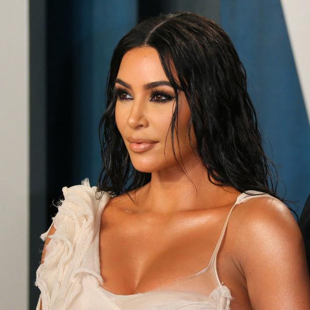Kim Kardashian bei einer Veranstaltung, mit dunklem, gewelltem Haar und einem hellen Kleid.