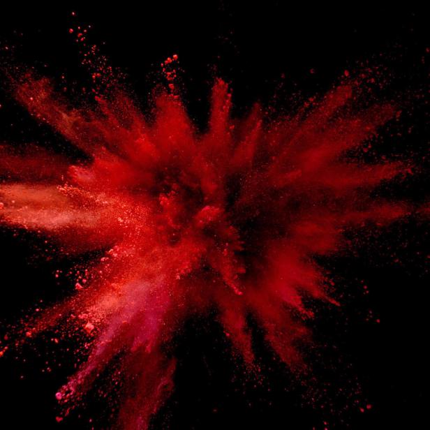 Eine rote Farbpulverexplosion vor einem schwarzen Hintergrund.