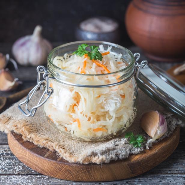 Ein Glas mit Sauerkraut und Karotten steht auf einem Holztisch.