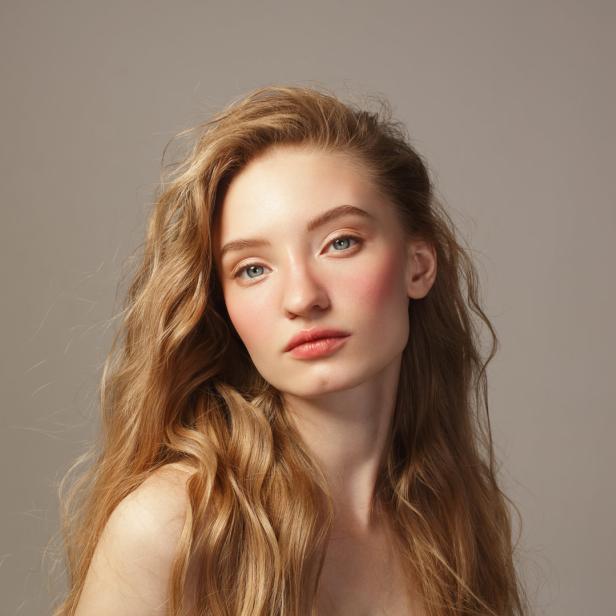 Porträt einer jungen Frau mit langen, gewellten blonden Haaren und zartem Make-up.